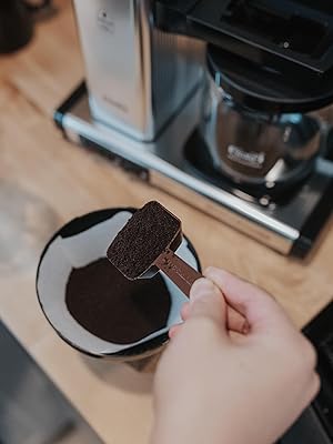 person scooping ground coffee into a Moccamaster brew basket
