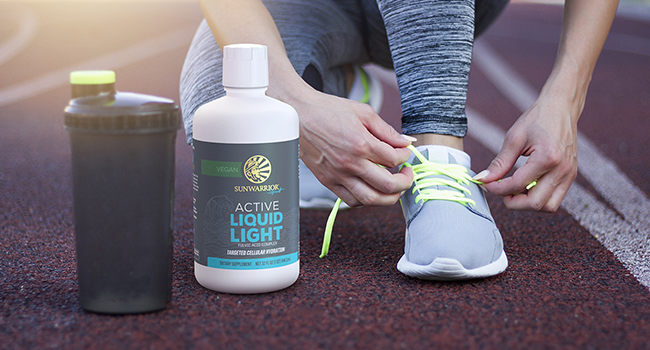 A bottle of Sunwarrior Active Liquid Light next to a woman tying her running shoes on a track.
