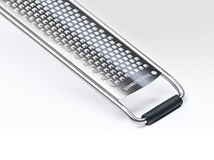 Close-up of a stainless steel grater with fine perforations. Features an ergonomic black handle and curved sides for stability.