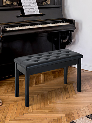 Black upright piano with bench featuring padded black cushioned seat and wood-tone frame legs positioned on wooden floor.