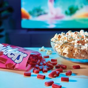 A bag of Twizzlers Nibs with candy pieces spilling out next to a bowl of popcorn