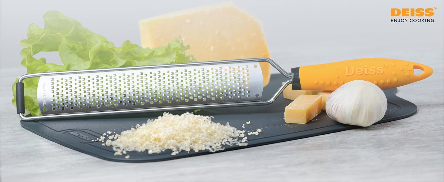 Kitchen grater with yellow handle on dark surface, surrounded by cheese, garlic, and lettuce. Grated cheese visible on board.