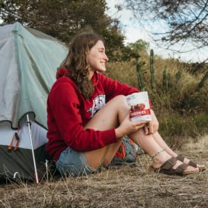 Woman holding bag of dried cherries as she sits outside of her camping tent in nature