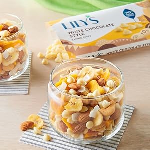 A bag of Lily's white chocolate style baking chips open and placed behind cups of trail mix