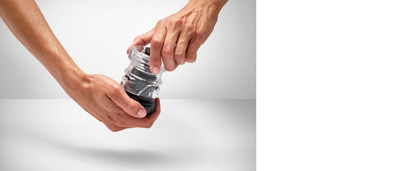 Hands gripping and applying dark-colored product to forearm skin. Close-up product application demonstration on person's arm against white background.