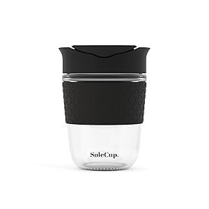 Text reads 'SoleCup.' Reusable coffee cup with two-tone design featuring white bottom section, black middle band with grip texture, and black top lid with ventilation slot.
