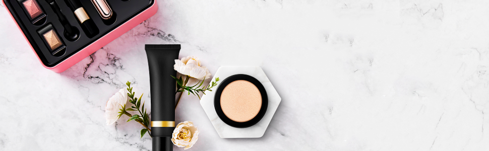 Cosmetic products arranged on a marble surface: black tubes, a hexagonal compact, and makeup brushes next to a pink rose.