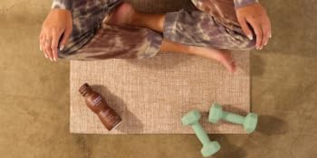 A woman on a yoga mat with light dumbbells, sipping a bottle of ICONIC protein shake.