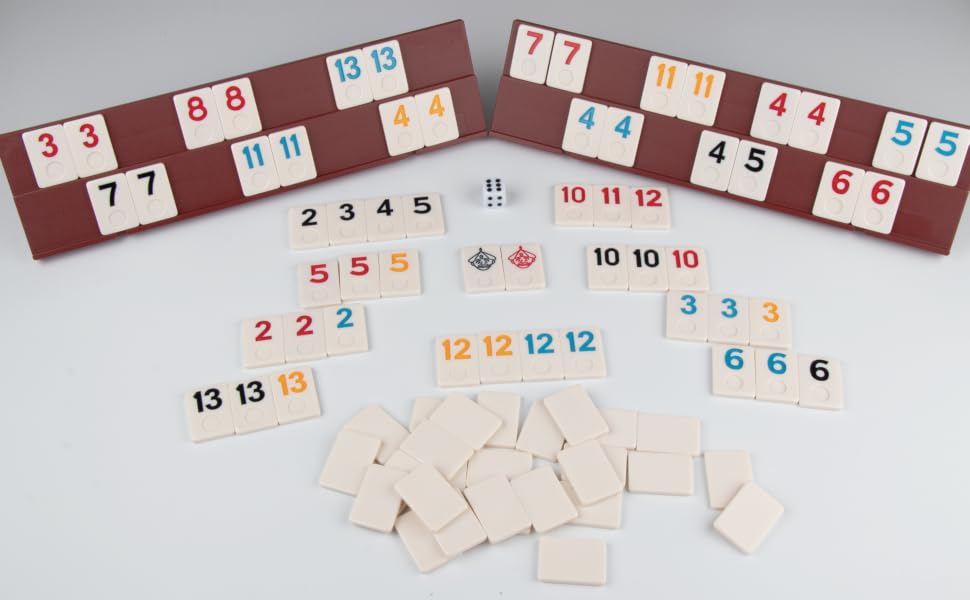Rummikub-style game pieces including numbered tiles in various colors, two game boards, and dice spread out on a white surface.