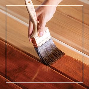 painter brushing on light brown stain on wood