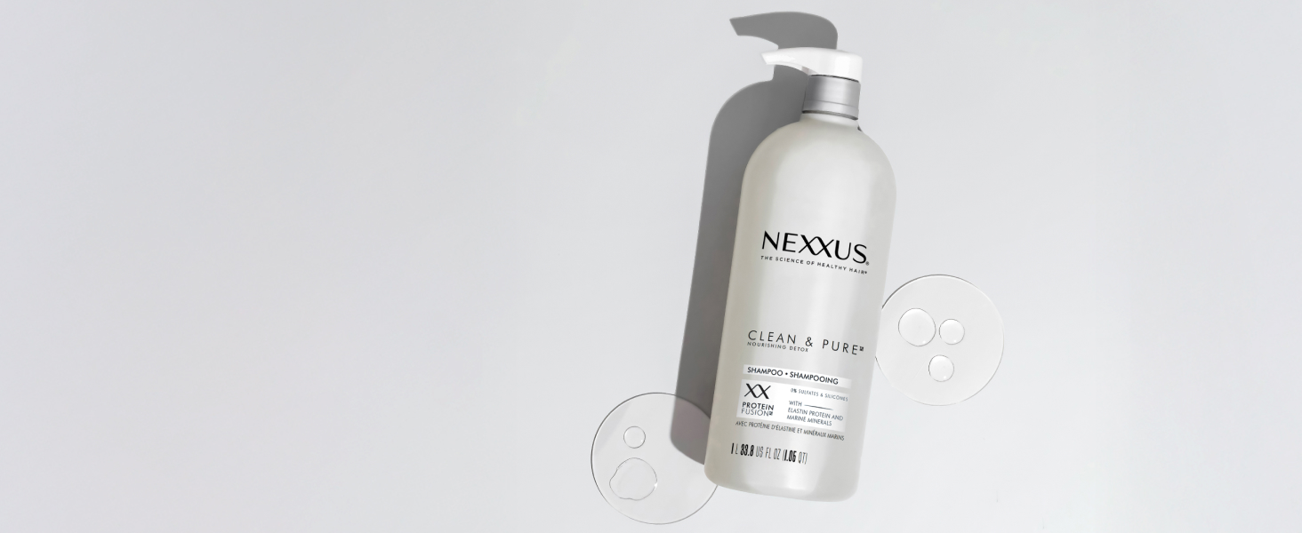 Nexxus Clear &amp; Pure shampoo pump bottle laying down on a white surface with drops on both sides.