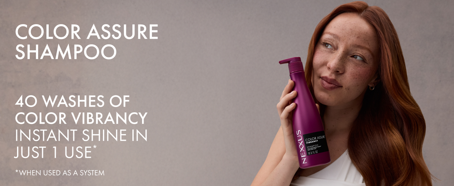 Young woman with vibrant wavy red hair holding a Nexxus Color Assure Shampoo bottle in one hand.
