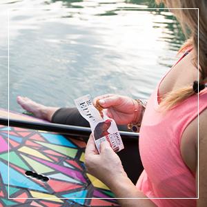 Woman eating an EPIC grass fed protein bar while sitting on a paddle board
