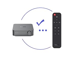 Compact media streaming device shown with matching remote control. Device features dark grey finish and minimalist design with wireless connectivity indication.