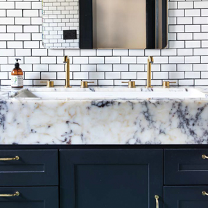 A sink with a marble countertop and brass faucet with blue cabinet doors and white tile