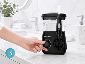 Hand operating black kitchen appliance, appears to be food processor or grinder. White modern kitchen setting visible in background.