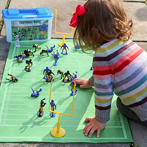 A girl playing with the play and black football players on roll out field.