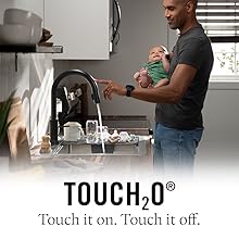 image of a father holding a baby while touching on a kitchen faucet