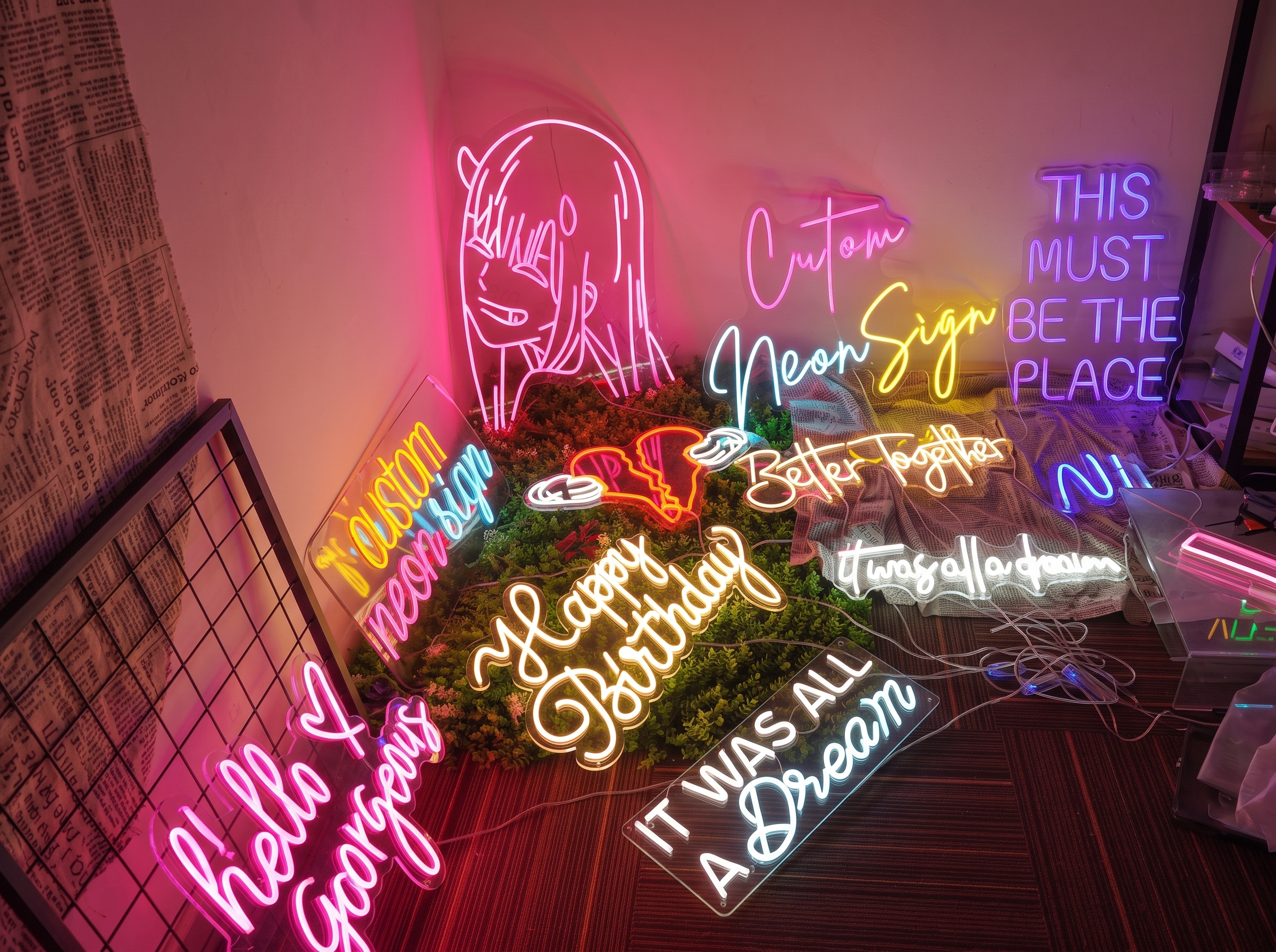 Colorful custom neon signs with anime artwork and handwritten phrases arranged across a studio floor.

