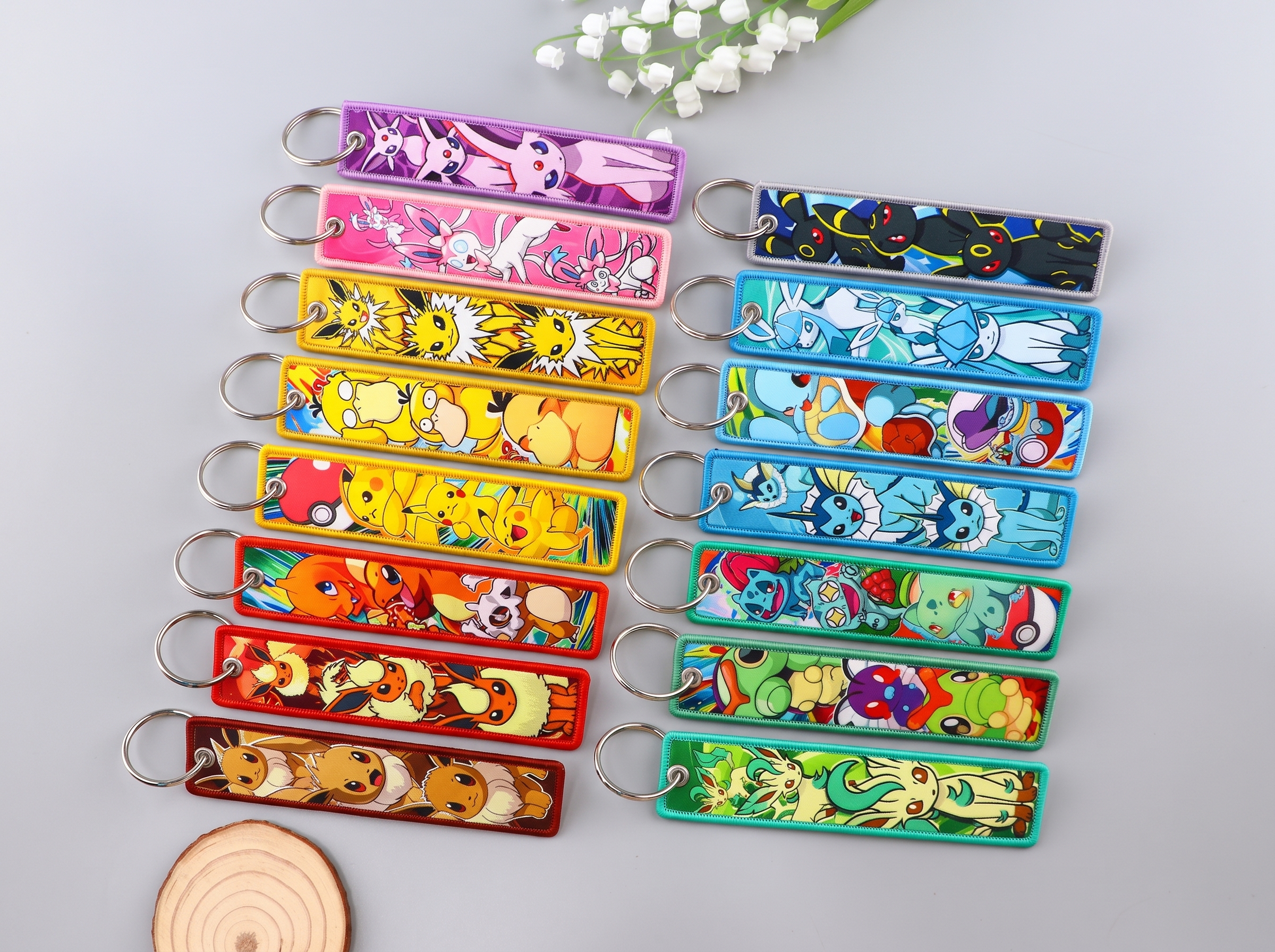 Colorful embroidered keychains featuring cartoon creatures arranged in two rows on a light gray surface.
