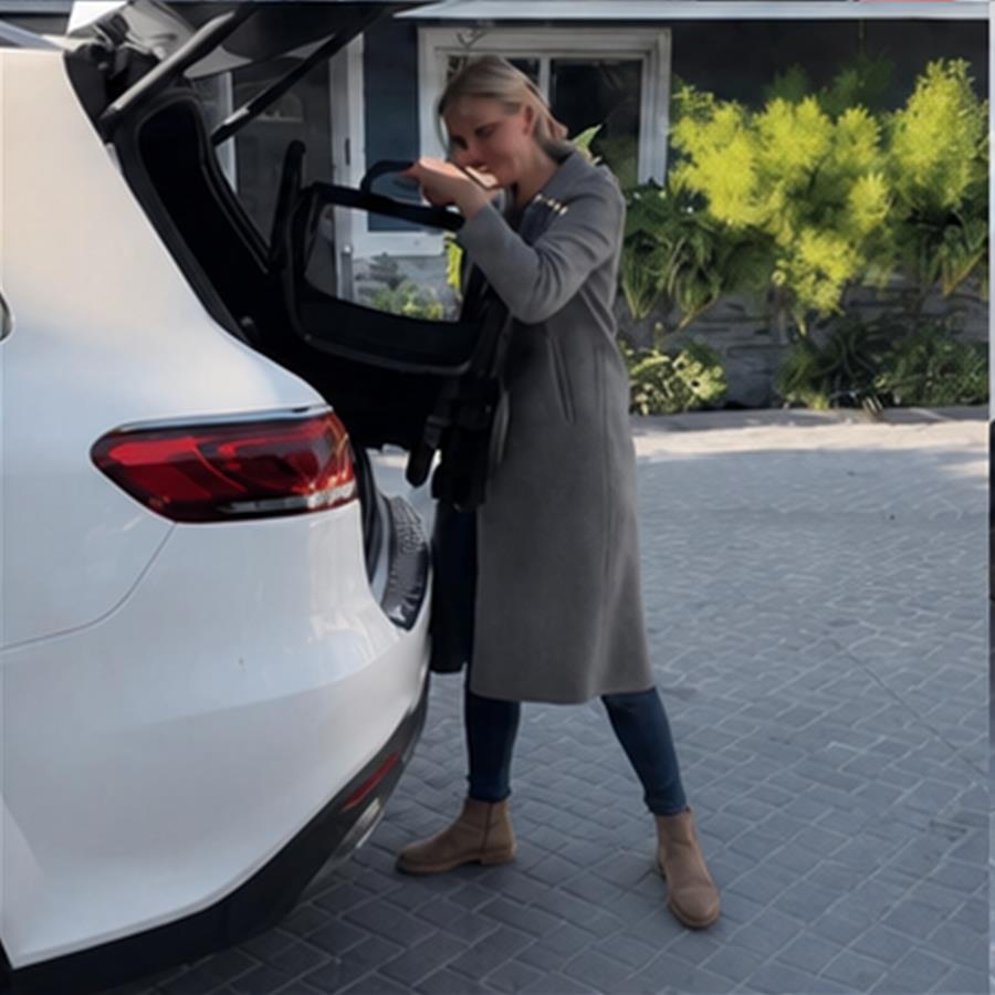 Owner folding the stroller frame beside the open boot of a compact car