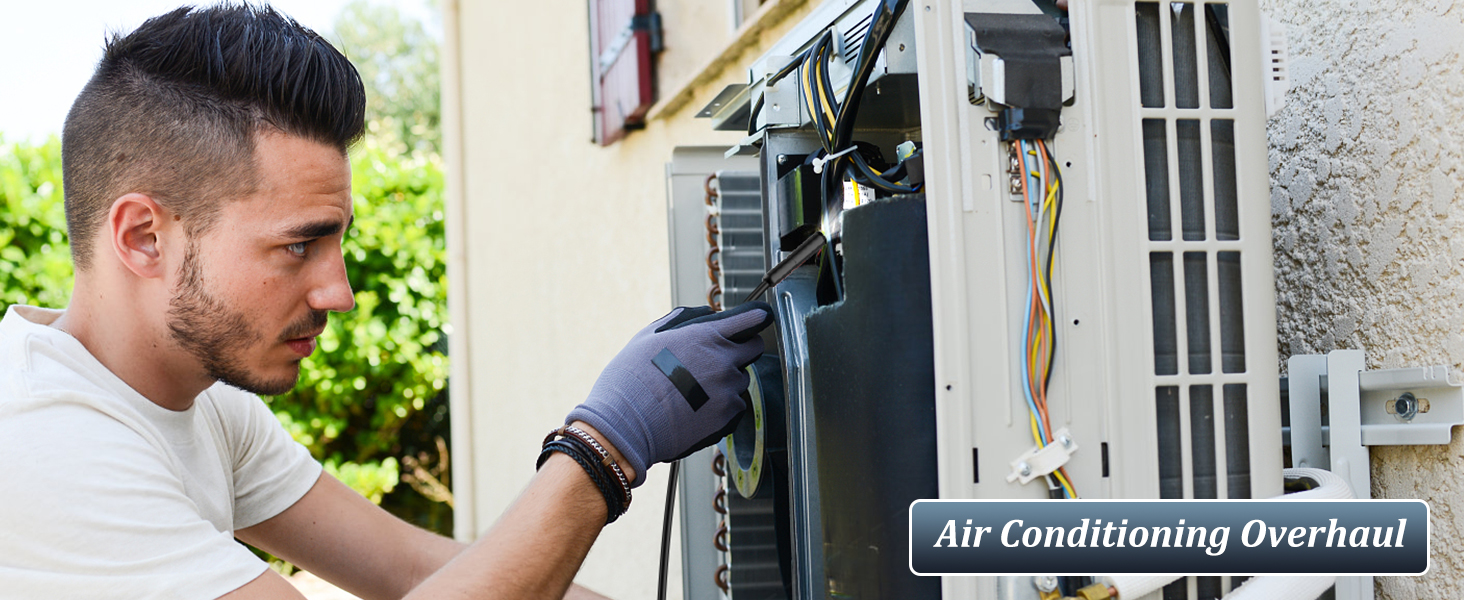 HVAC technician performing maintenance on an outdoor air conditioning unit, wearing protective gloves while examining components during an overhaul service.