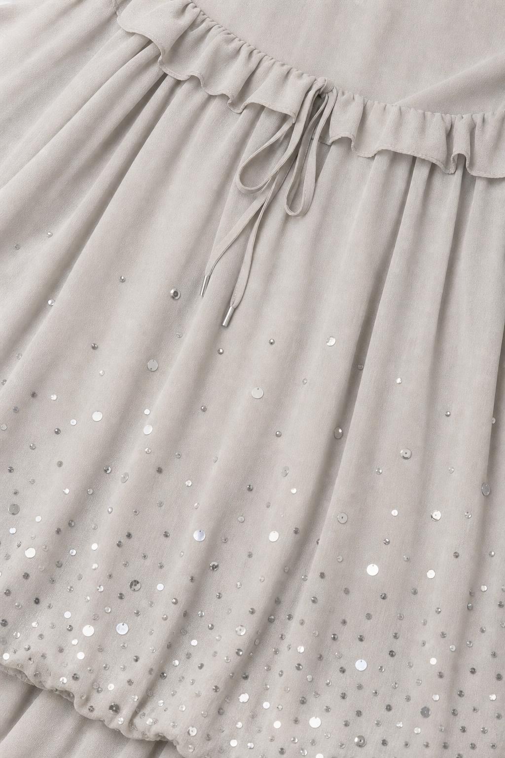 Close-up detail of sequin embellishments and drawstring waist on grey chiffon dress
