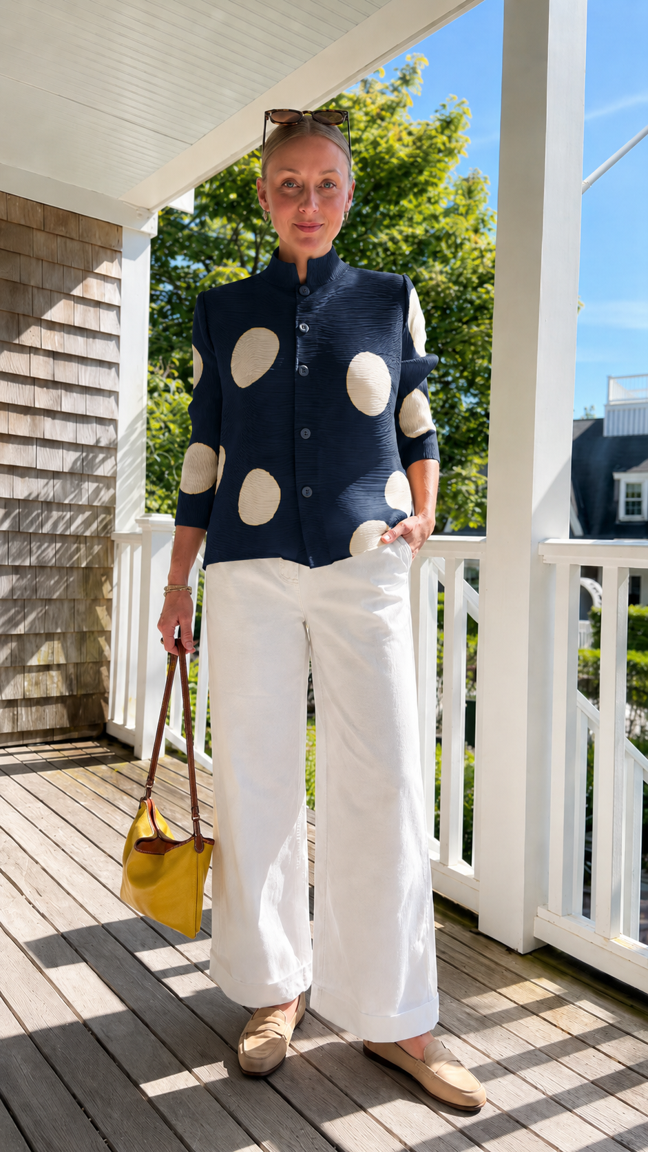 Front view of navy pleated polka dot button-front jacket top styled with white wide-leg pants