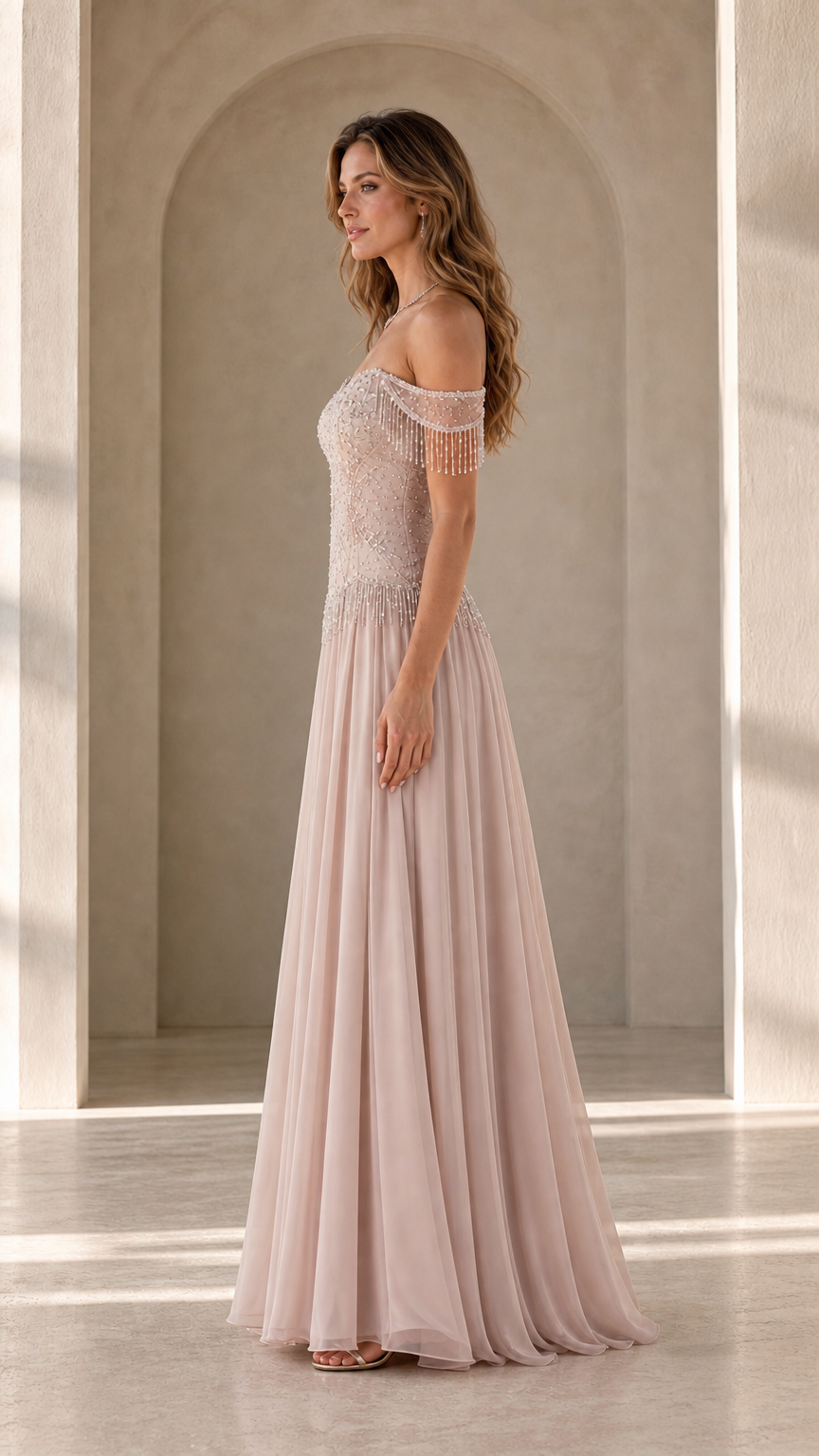 Side profile view of model in blush pink formal gown showing arm fringe detail
