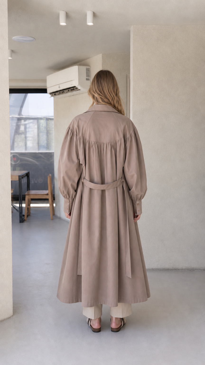 Back view of model wearing the taupe brown maxi trench coat showing gathered shoulder yoke and storm flap