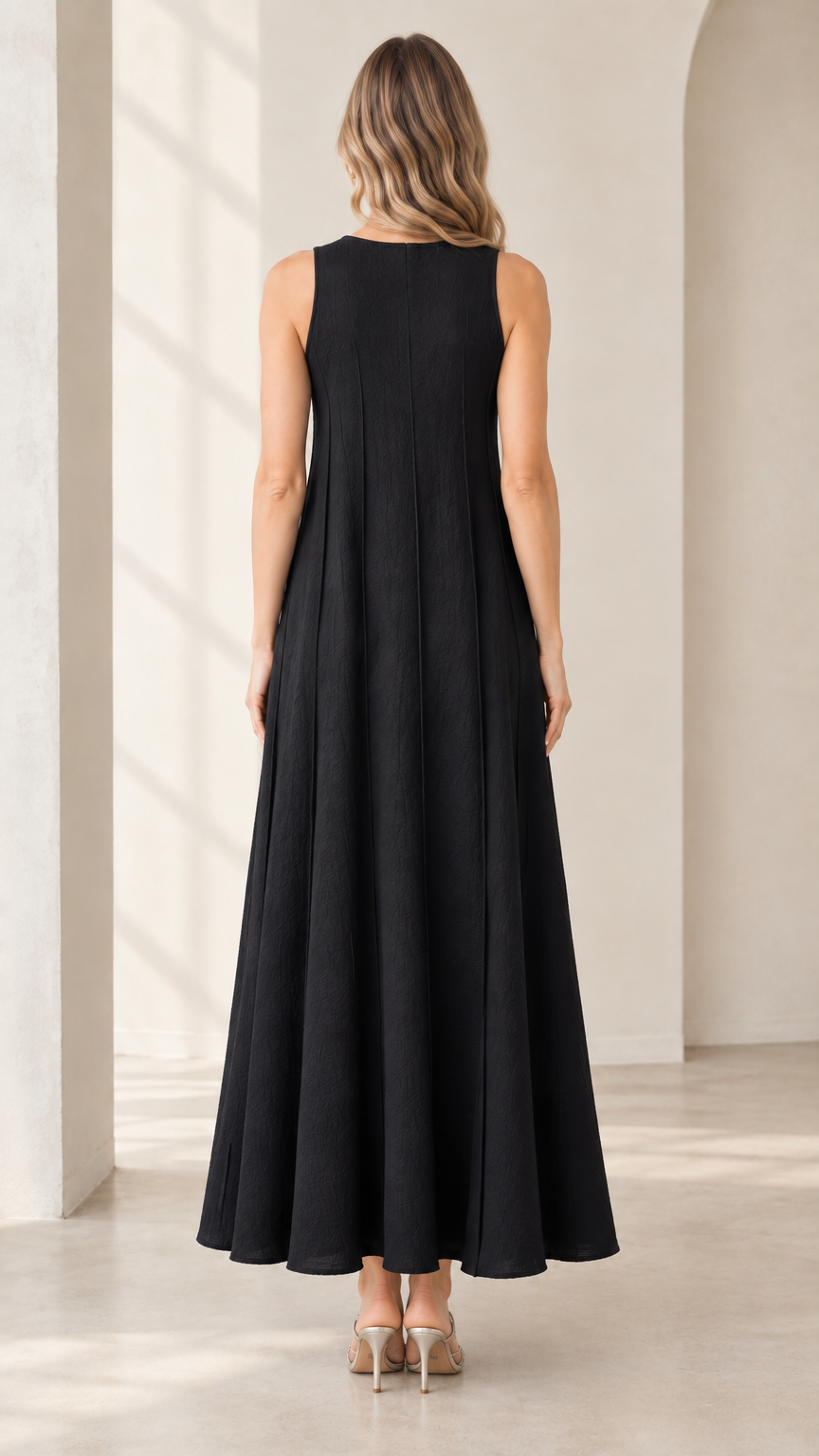 Back full-length view of woman wearing black sleeveless maxi dress showing vertical seam detailing