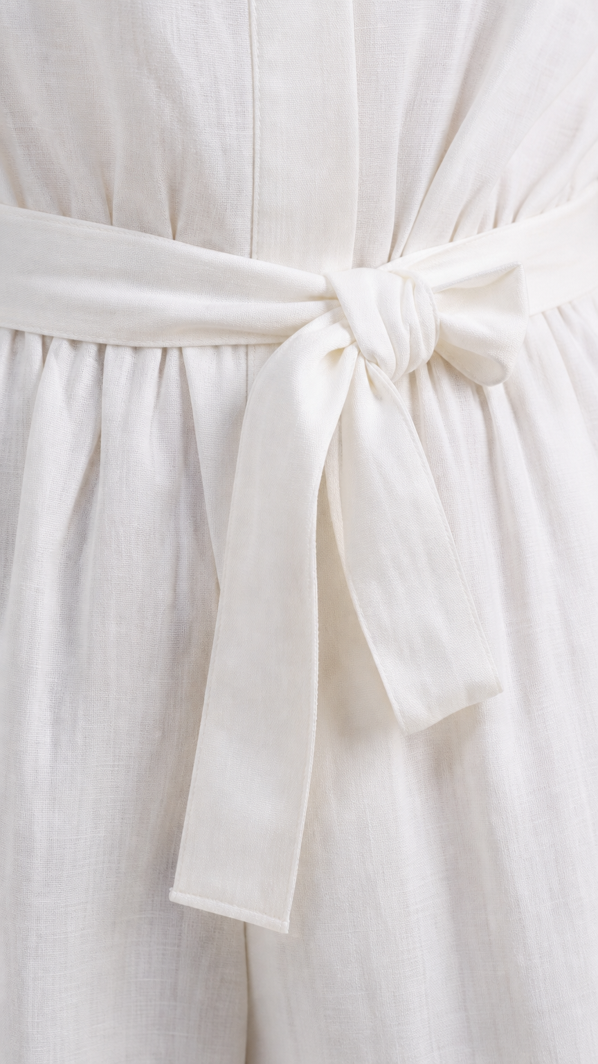 Close up view of white textured fabric and tied waist belt on jumpsuit