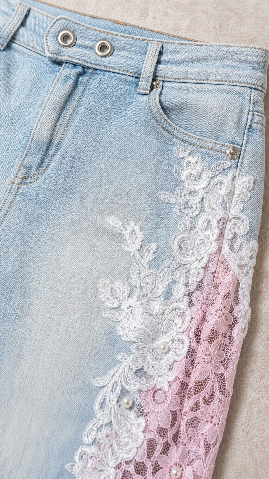 Close-up detail of light blue denim waistband, beaded floral embroidery, and lace insert