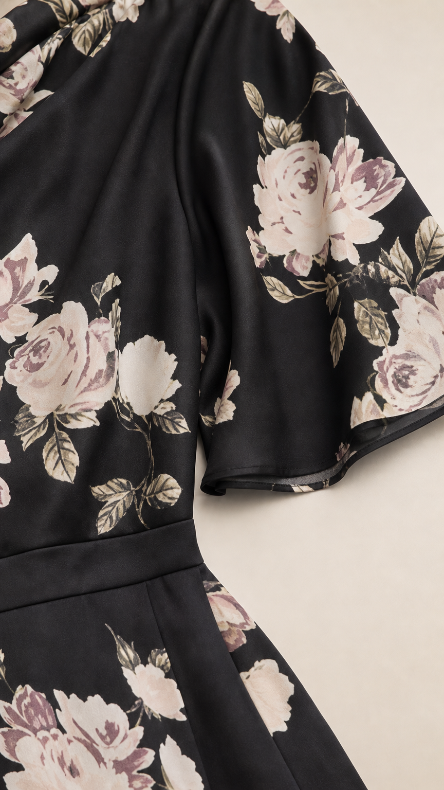 Close-up detail of black floral fabric, draped shoulder, and flutter sleeve