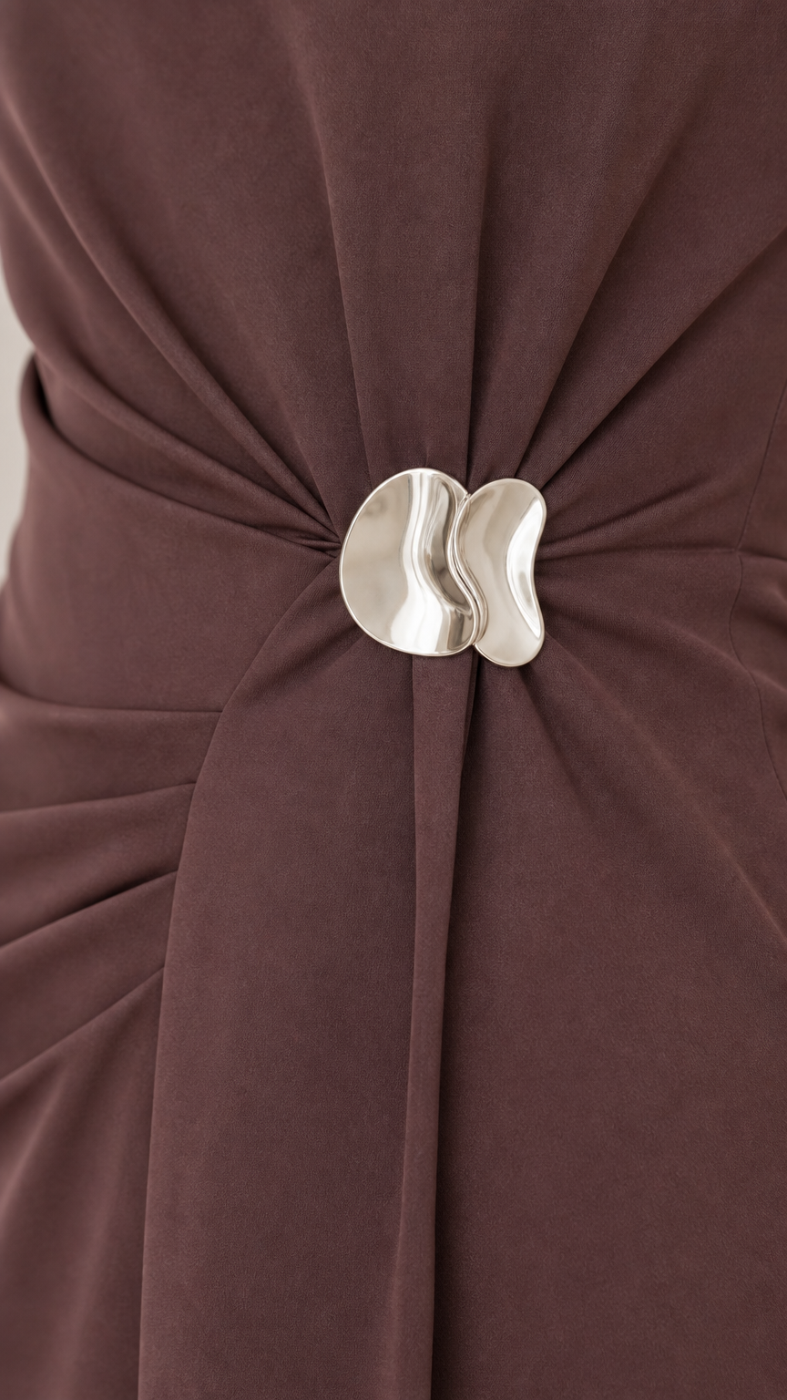 Close-up detail of gathered waist pleats with sculptural silver metallic buckle on brown dress