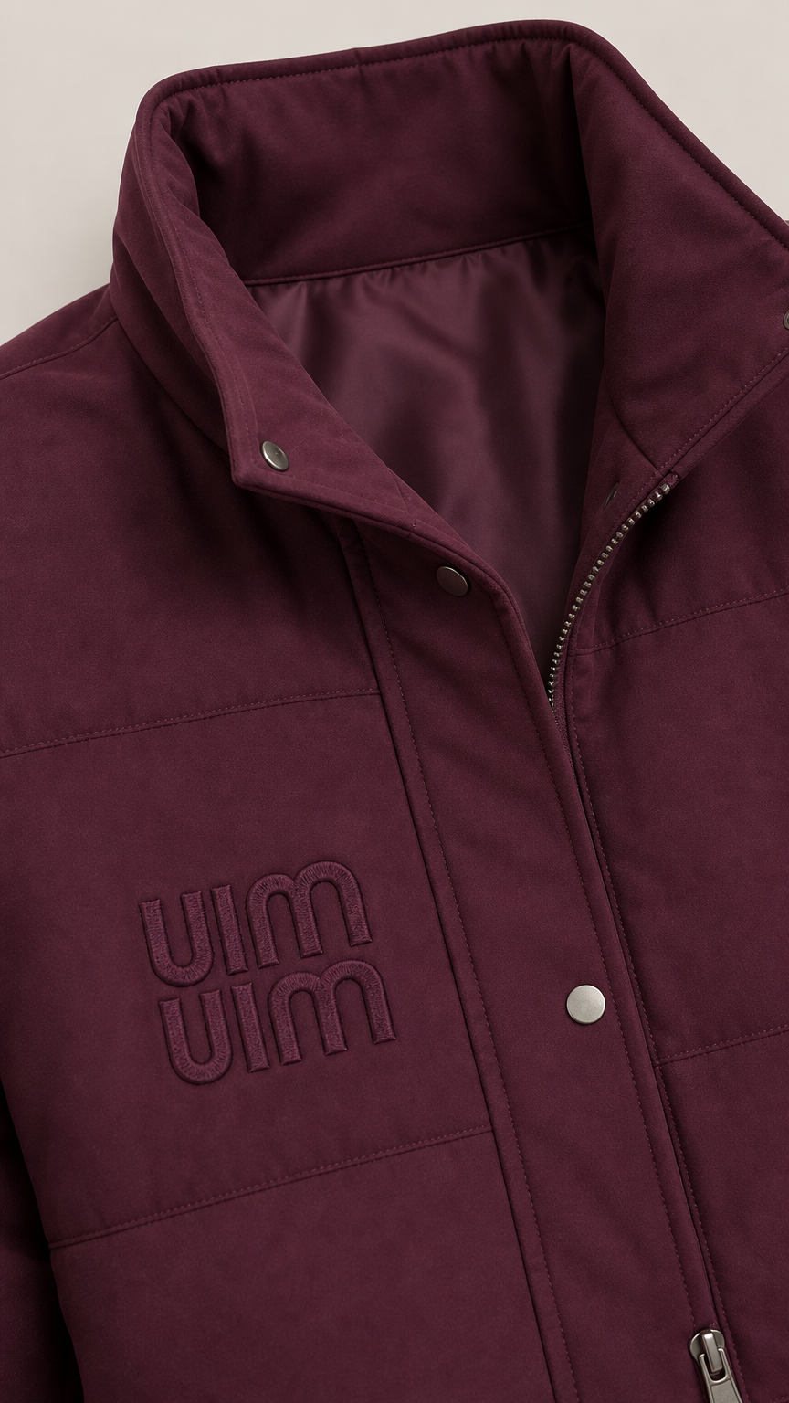 Close-up detail of burgundy stand-collar puffer vest with snap buttons, zipper, and subtle chest embroidery