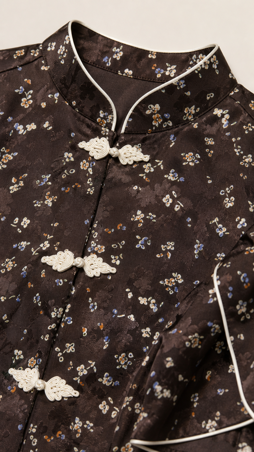 Close-up of Mandarin collar, white piping, and frog closures on dark brown floral fabric