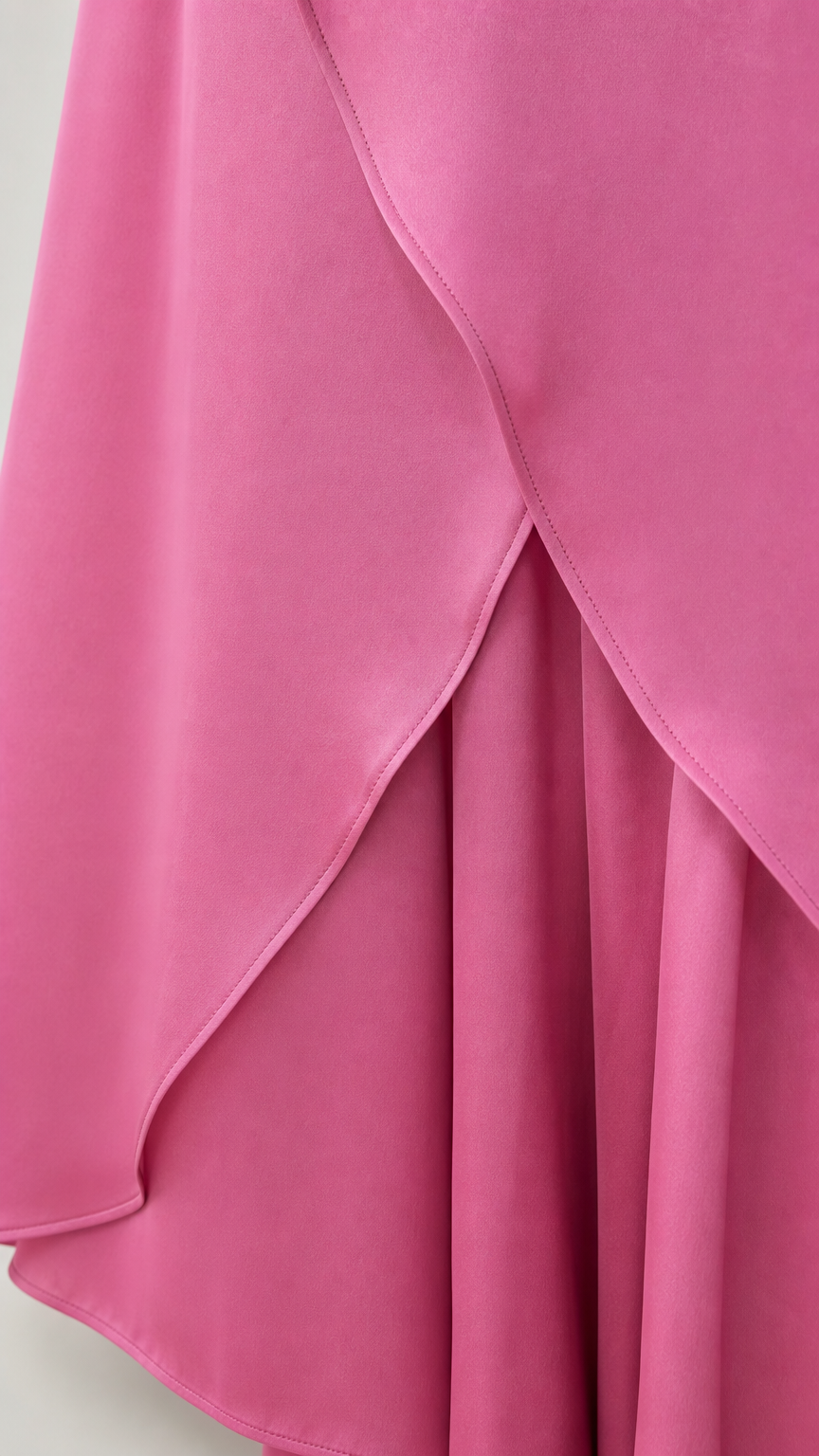 Close-up detail of smooth-draped fuchsia pink layered fabric and curved tulip hem finish