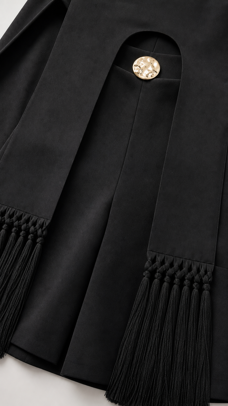 Close-up of black fabric, gold button detail, and tassel fringe hem