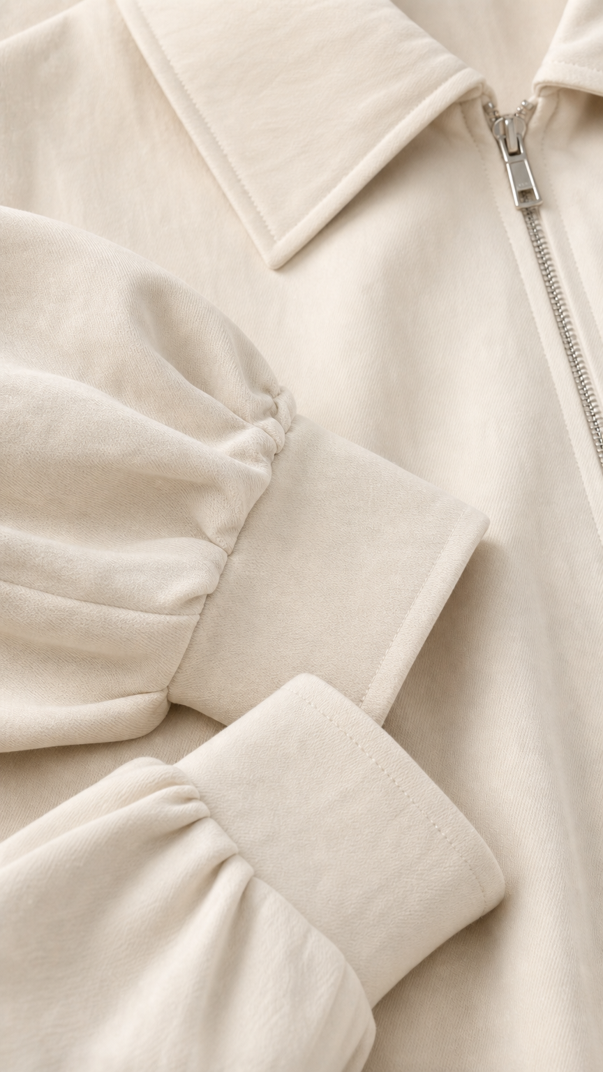 Close-up detail of cream jacket collar, metallic zipper, and gathered cuff