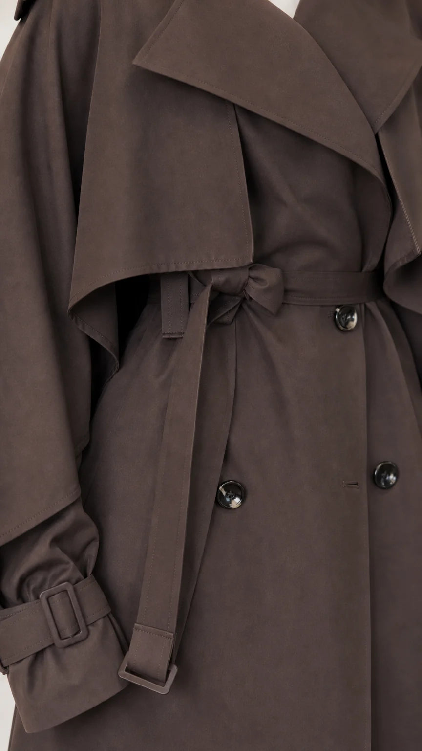 Close-up of dark brown trench coat cape overlay, belt buckle, cuff strap, and buttons
