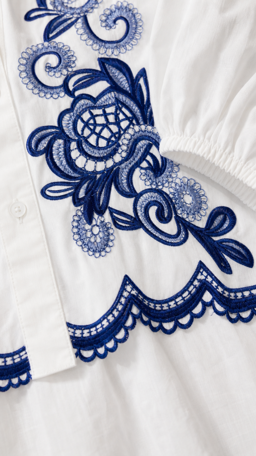 Close-up detail of blue embroidery and scalloped hem on white fabric