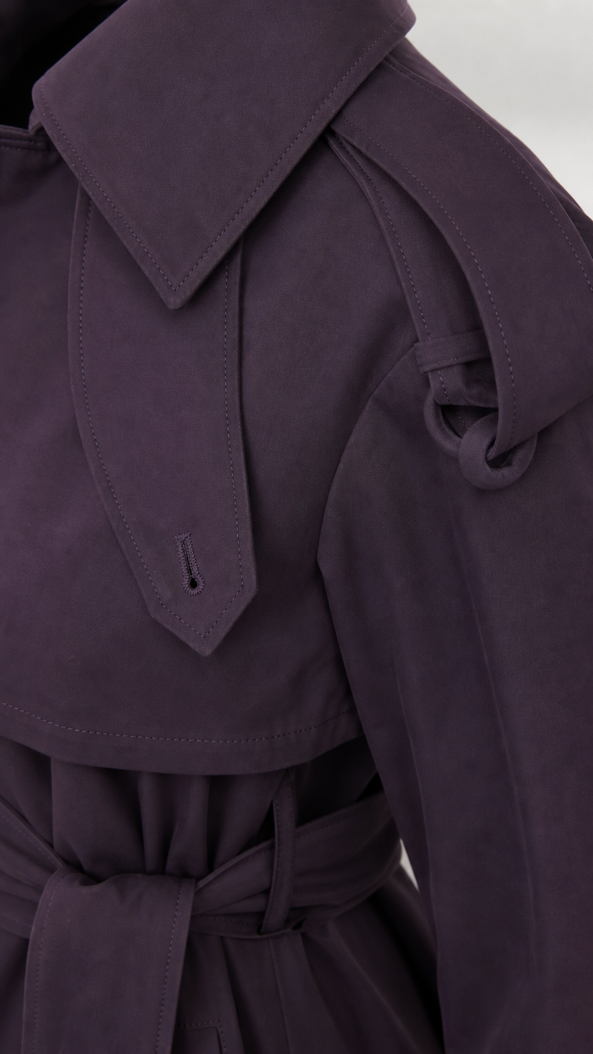 Close-up detail of deep purple trench coat shoulder epaulet tab and collar