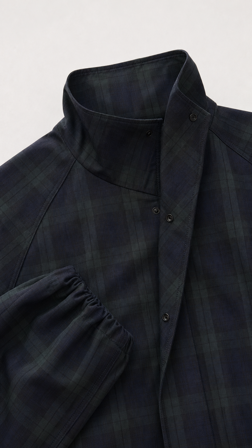 Close-up detail of the snap-button high stand collar and sleeve cuff on dark plaid jacket