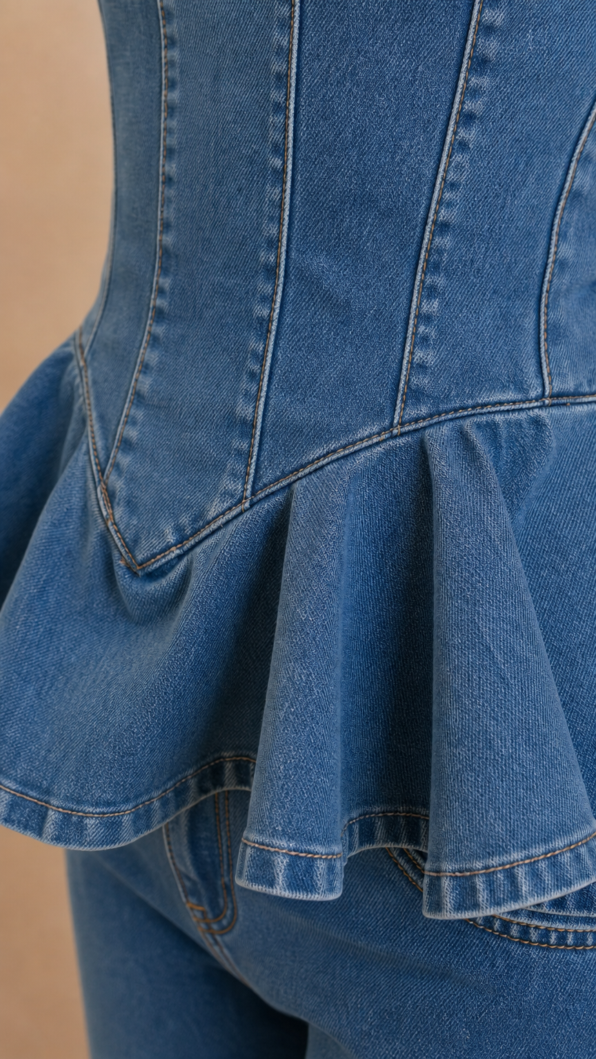 Close-up detail of structured corset seaming and flared peplum ruffle on blue denim top