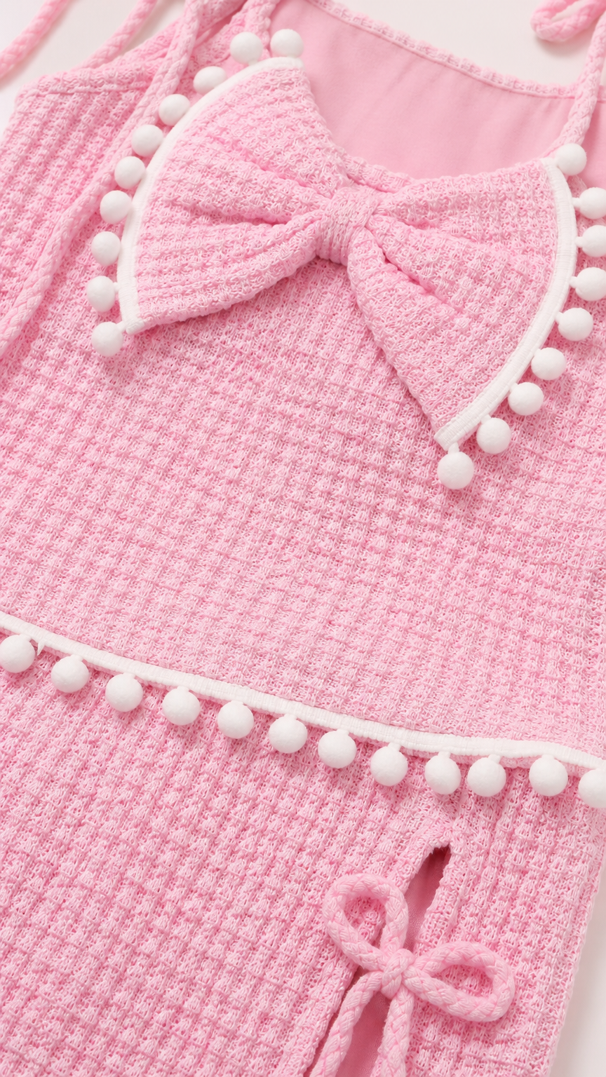 Close-up detail of pink textured knit fabric, bow accent, and white pompom trim