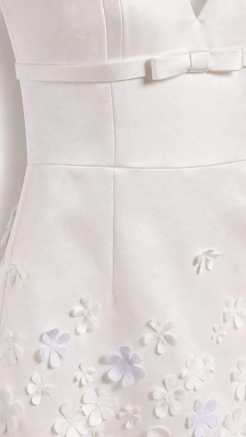 Close-up of white mini dress bodice bow and 3D floral hem