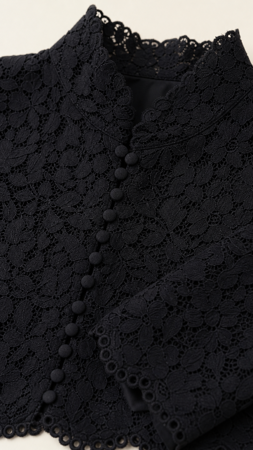 Close-up detail of black floral lace fabric, button placket, and scalloped high neckline