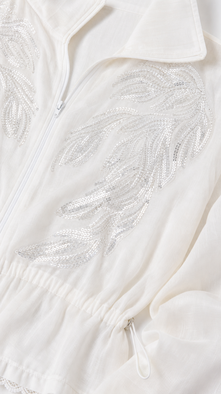 Close-up of intricate silver sequin leaf embroidery on white zip-up jacket