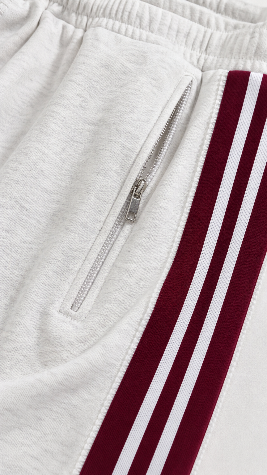 Close-up detail of white track pant zipper pocket and striped side trim